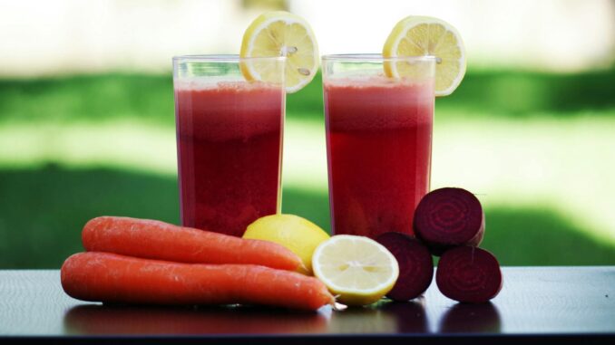 Colorful glasses of beetroot and carrot juice garnished with lemon slices, symbolizing health and freshness.