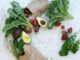 Top view of fresh avocados, kale, tomatoes, and peppers arranged on a marble surface.