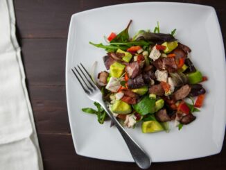 A fresh bacon, avocado, and mixed greens salad served on a square plate with a fork.